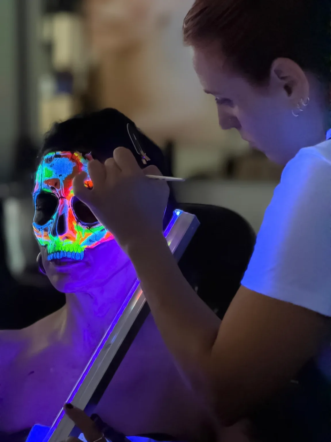 Tania Porcel realizando un maquillaje neón y glitter a una persona caracterizada como calavera
